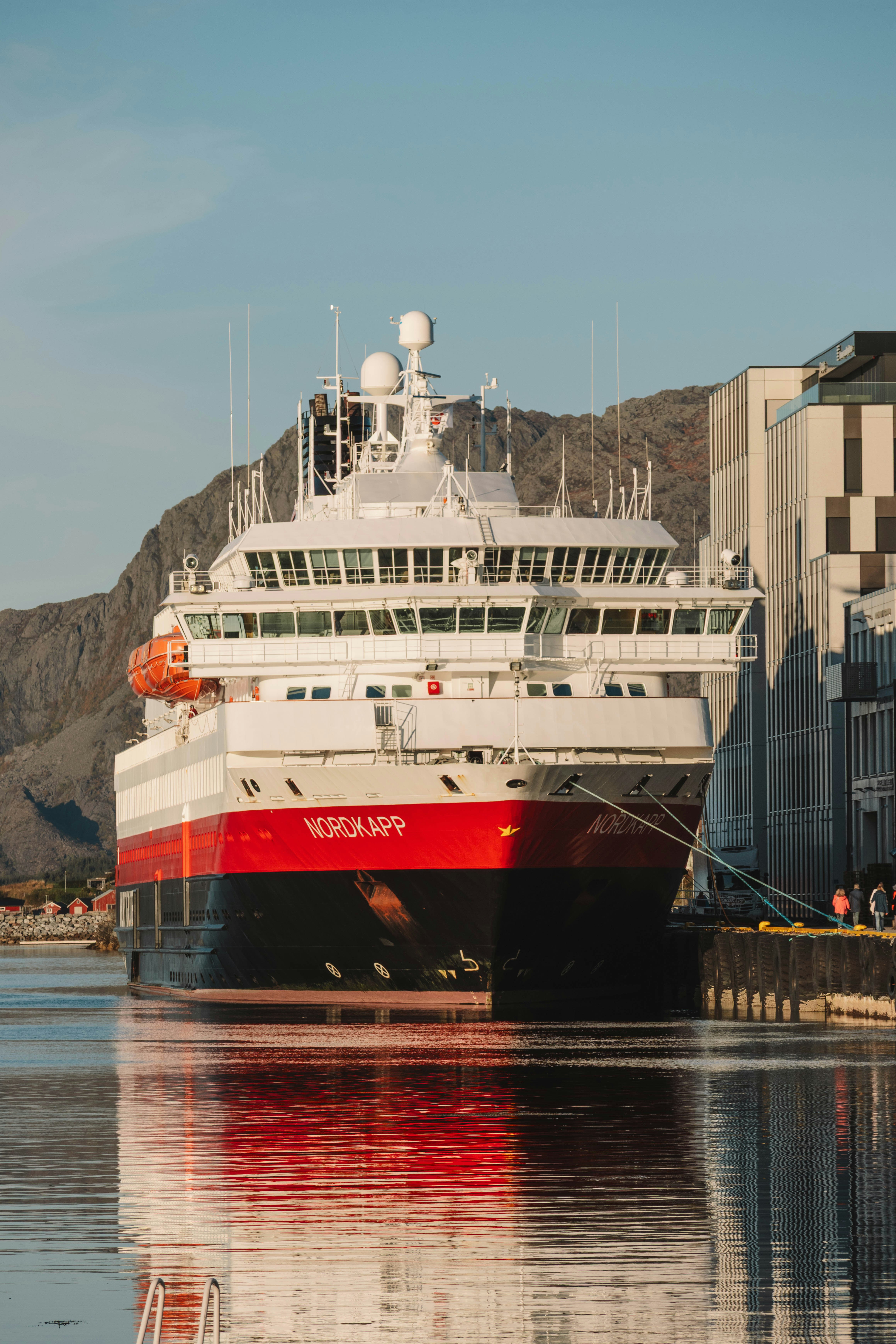 Large red and white ship docked by modern building