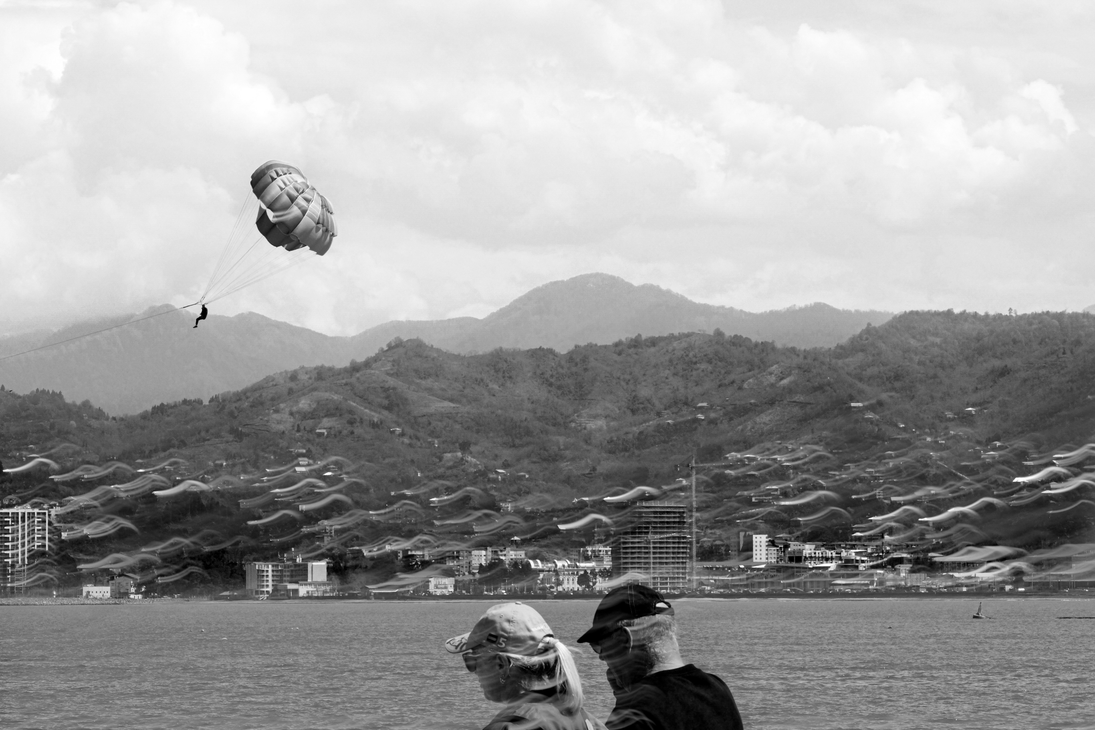 People watch parasailing with mountains in background.