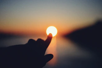 Finger touching the sun at sunset over water