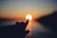 Finger touching the sun at sunset over water