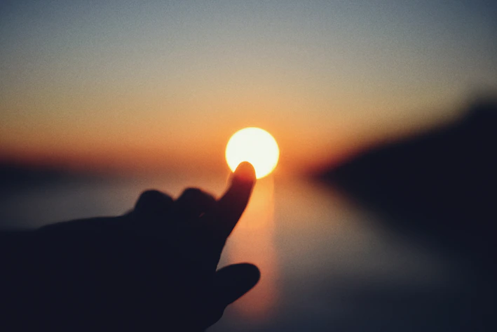 Finger touching the sun at sunset over water