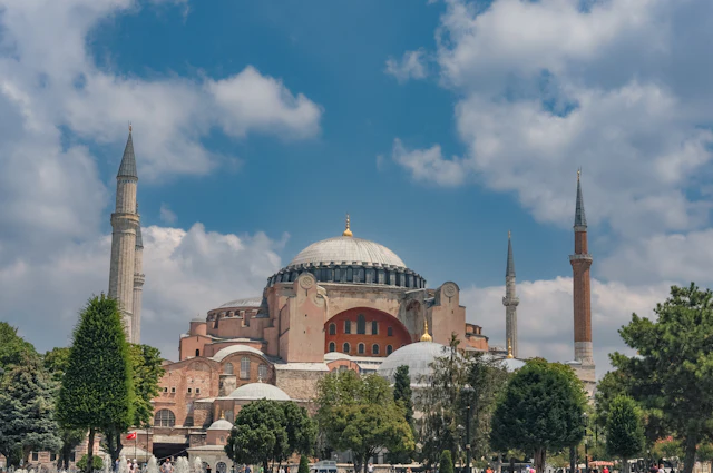 Hagia Sophia's dome and mismatched minarets rise above trees under a blue sky.