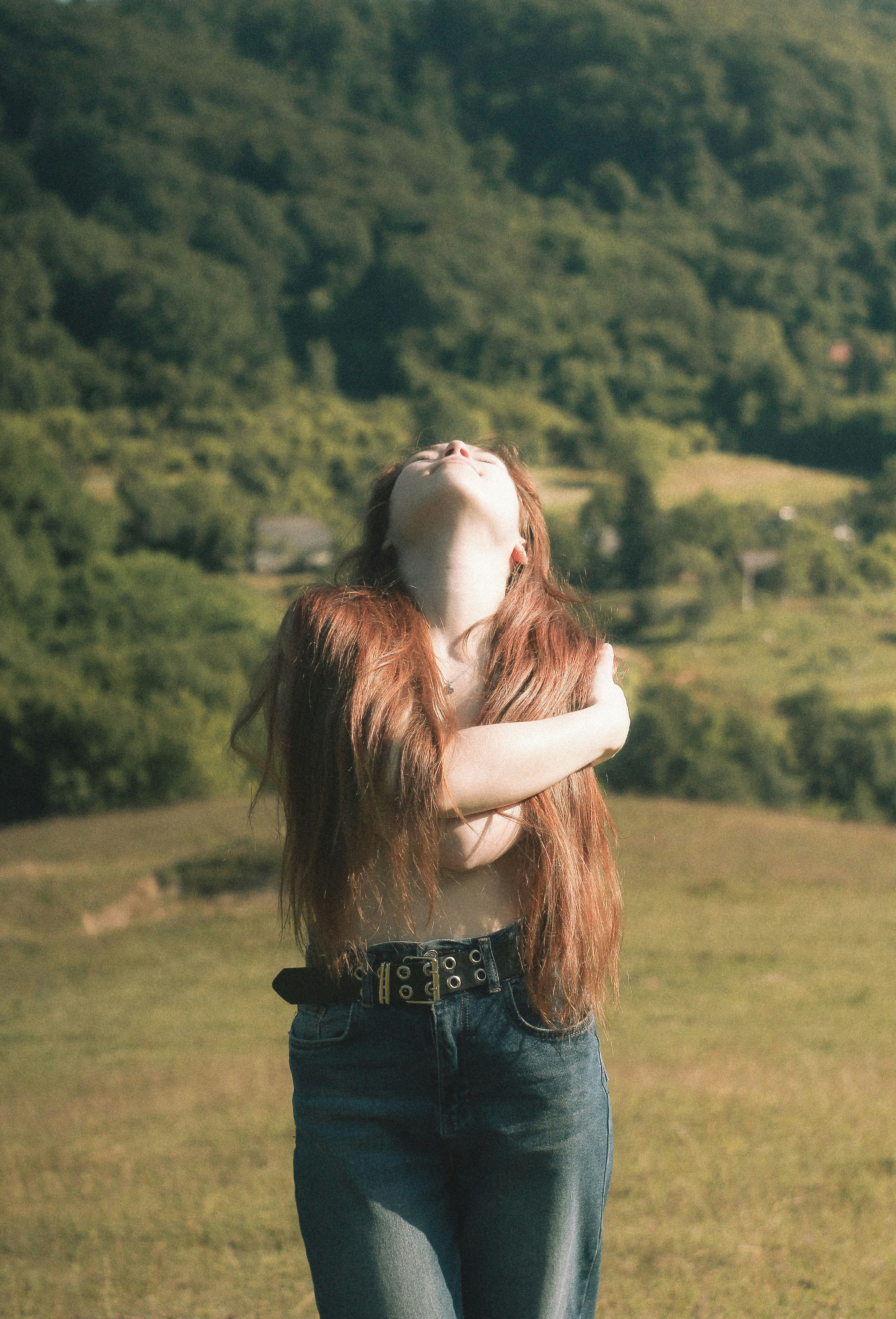 Woman with long red hair embraces herself outdoors.