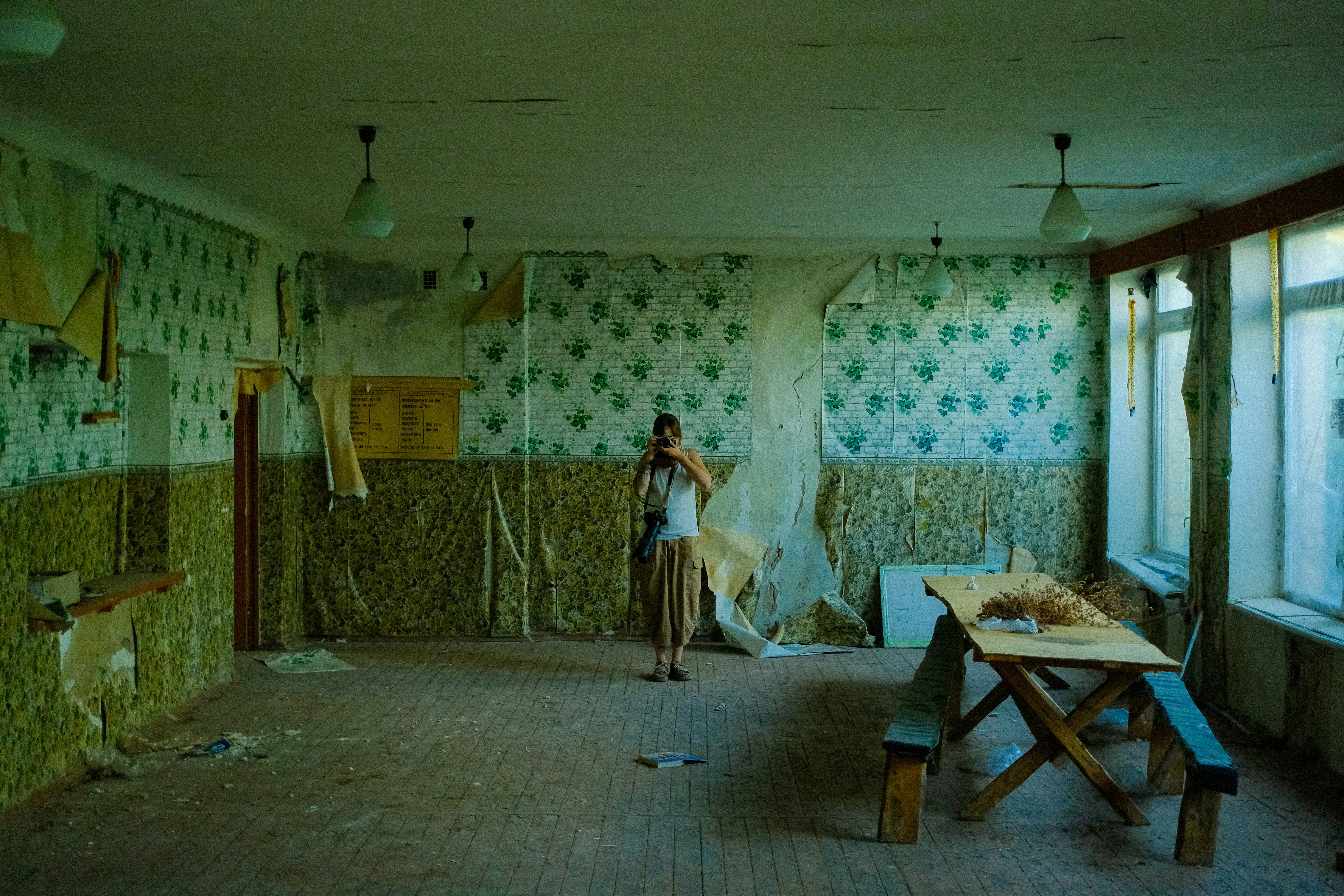 Person standing in a dilapidated room with peeling wallpaper.