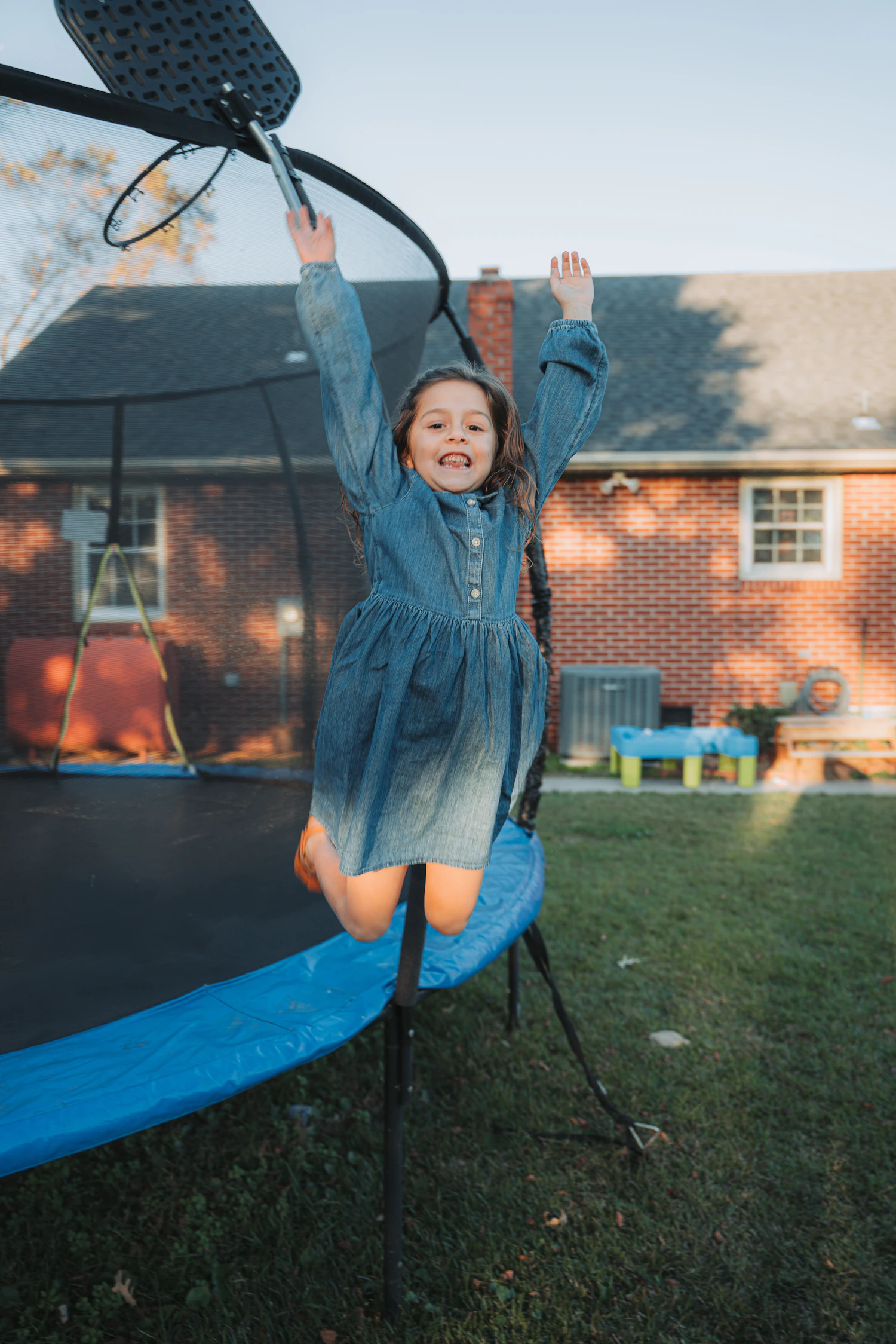 A young girl mid-air, laughing, jumping on a backyard trampoline