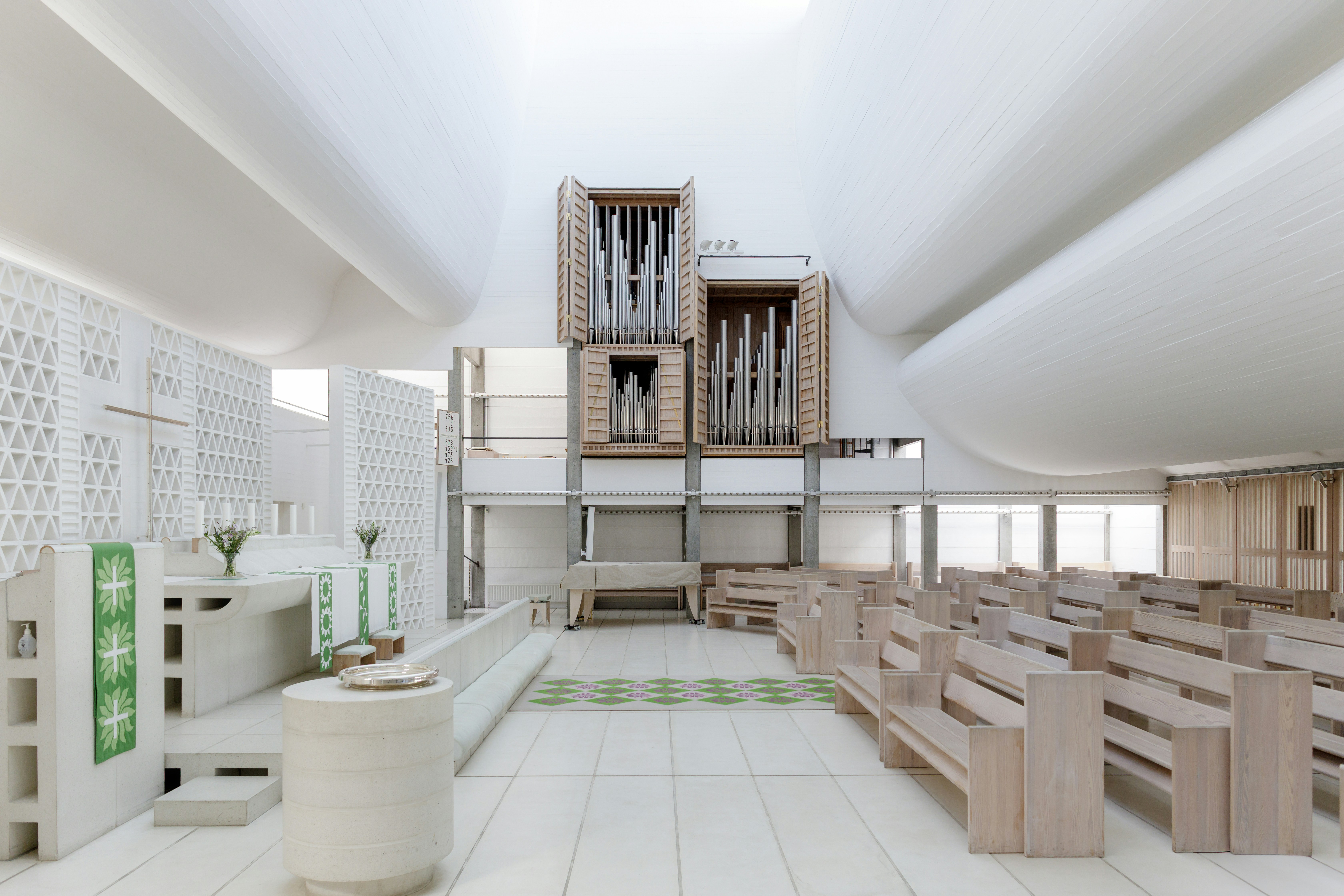 Modern white church interior with wooden pews and organ.