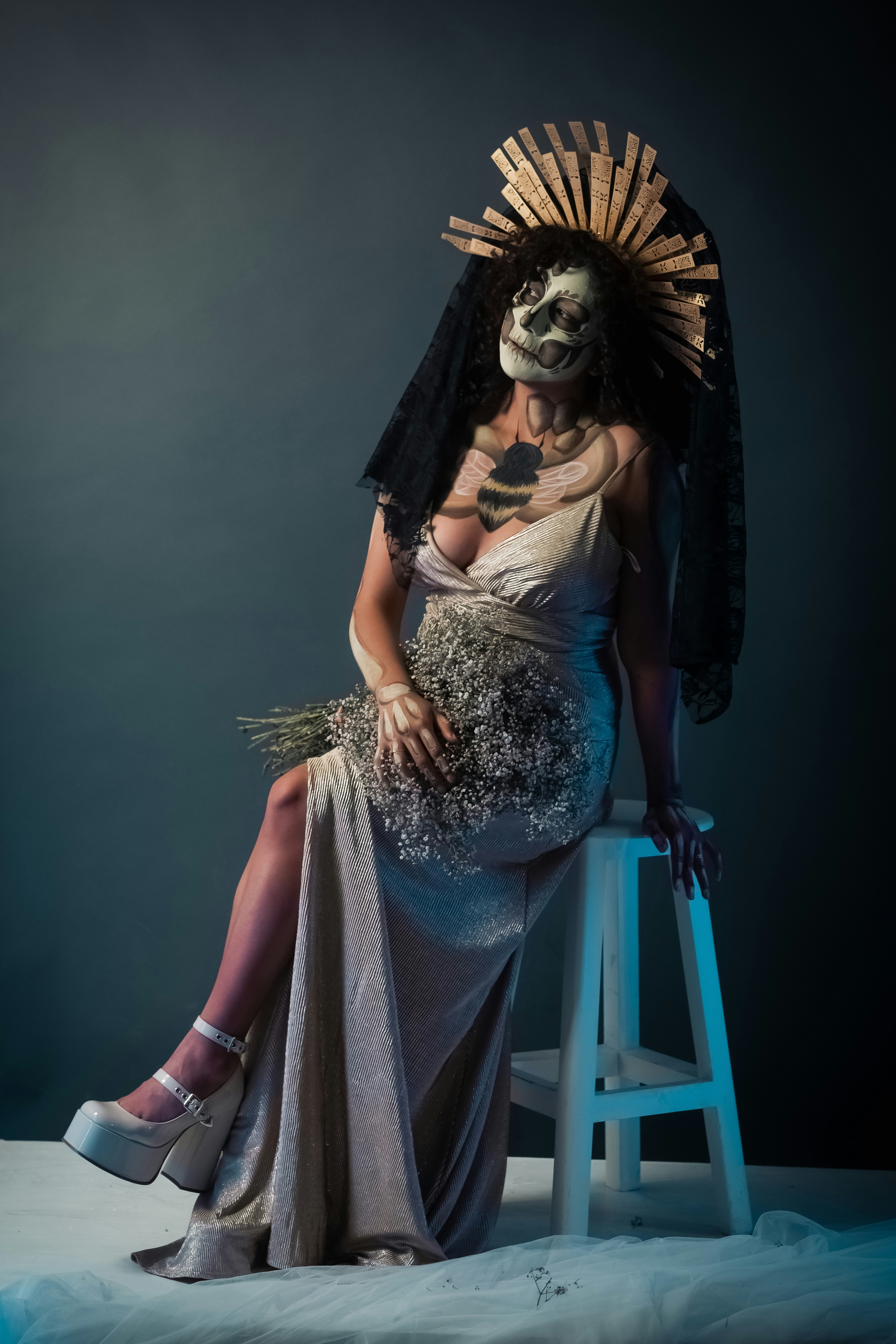 Mulher com maquiagem de crânio e cocar elaborado segurando flores.