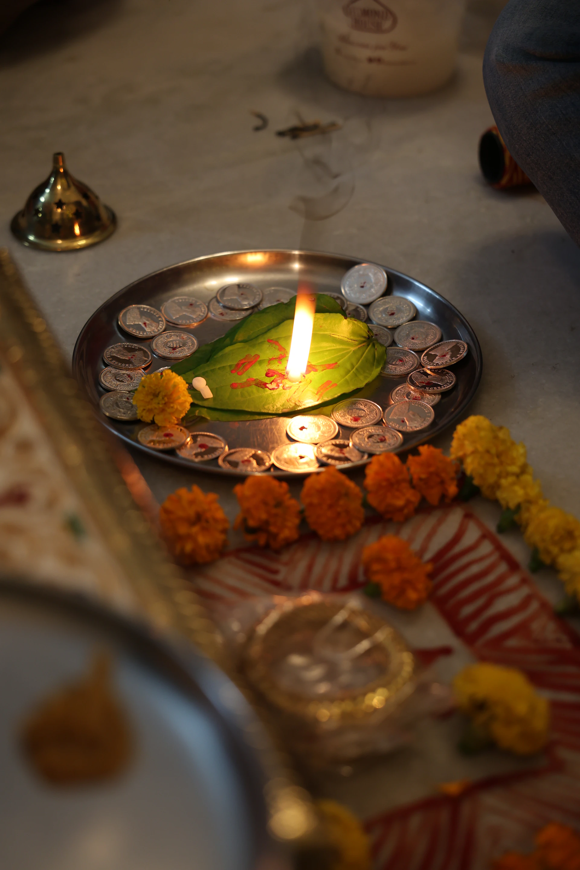 A lit candle on a plate with coins and flowers.