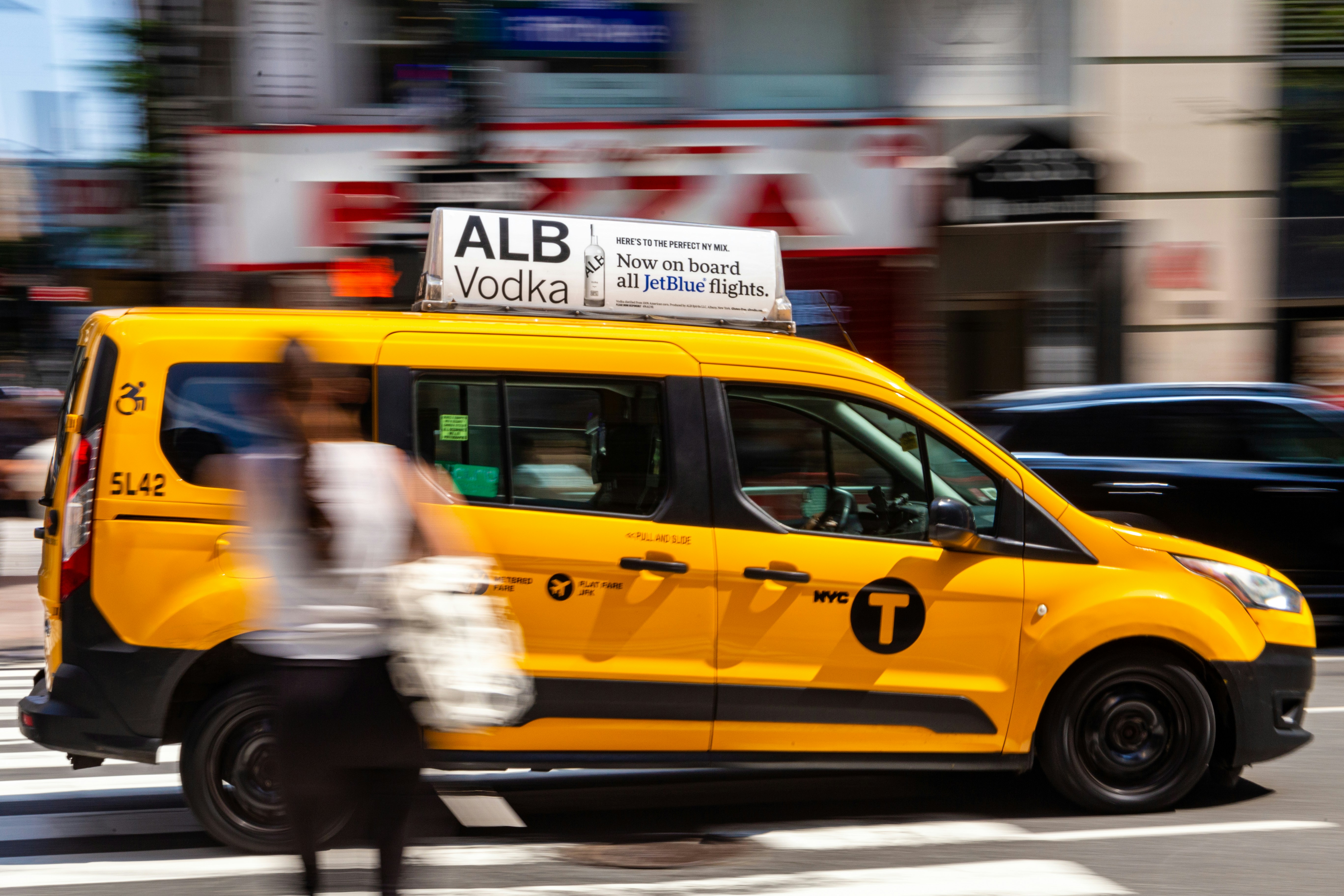 A yellow taxi cab drives down a blurred street.