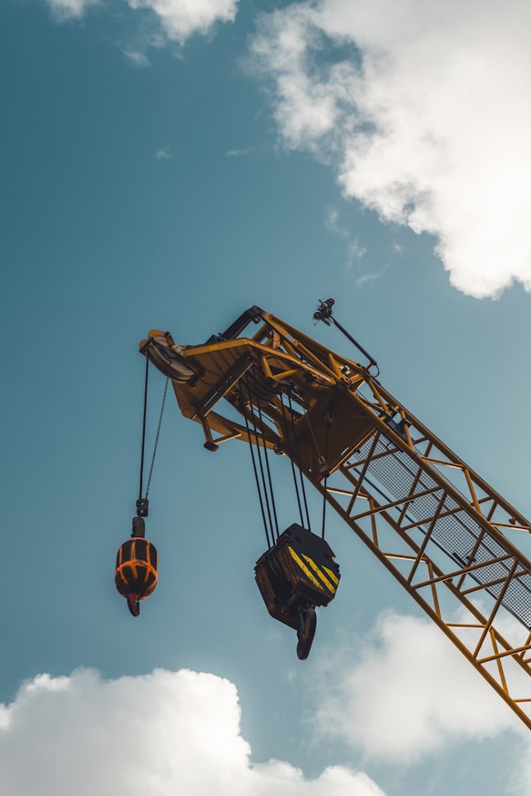Yellow crane boom with hooks against blue sky