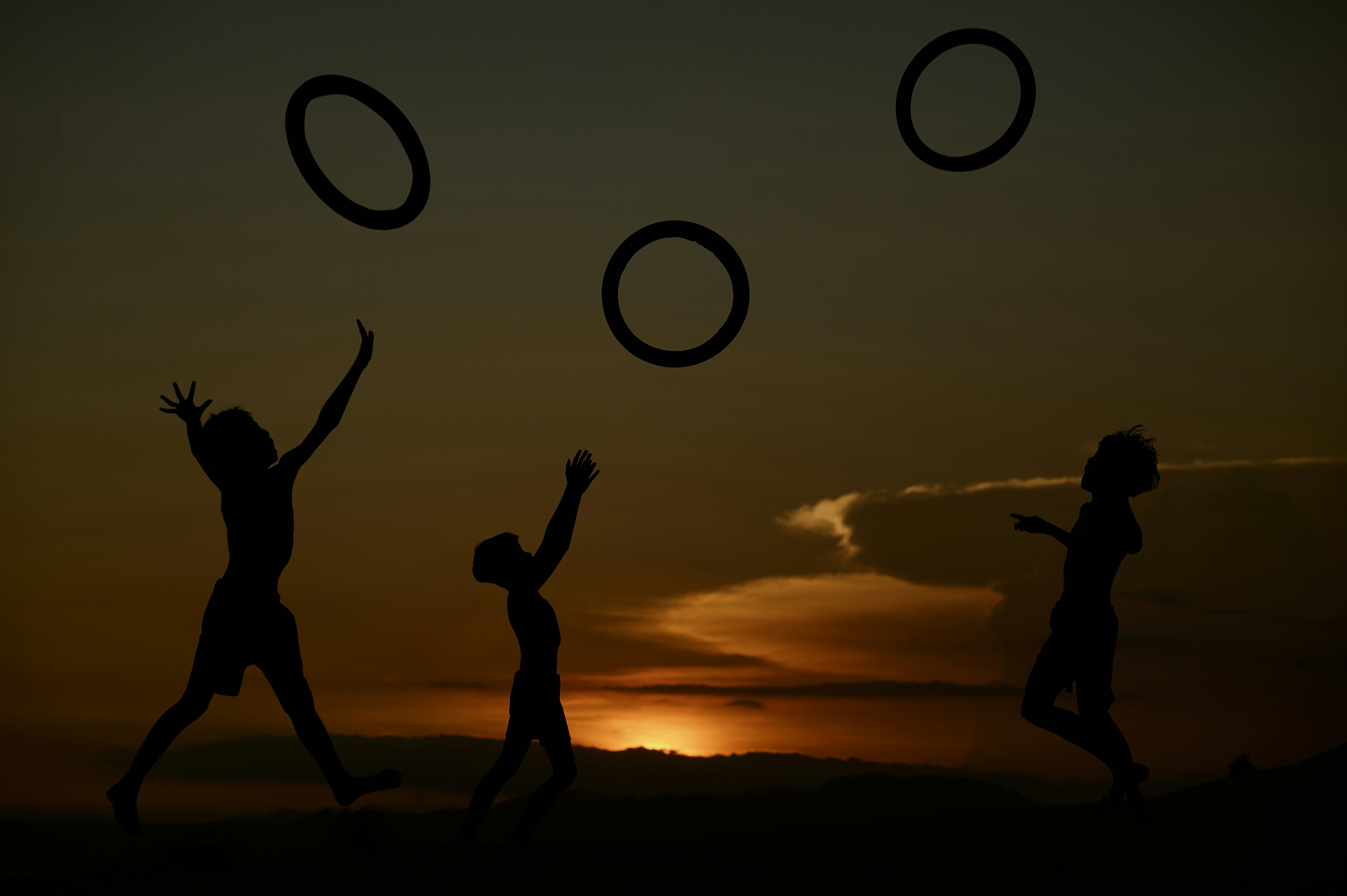Children silhouetted against sunset tossing rings
