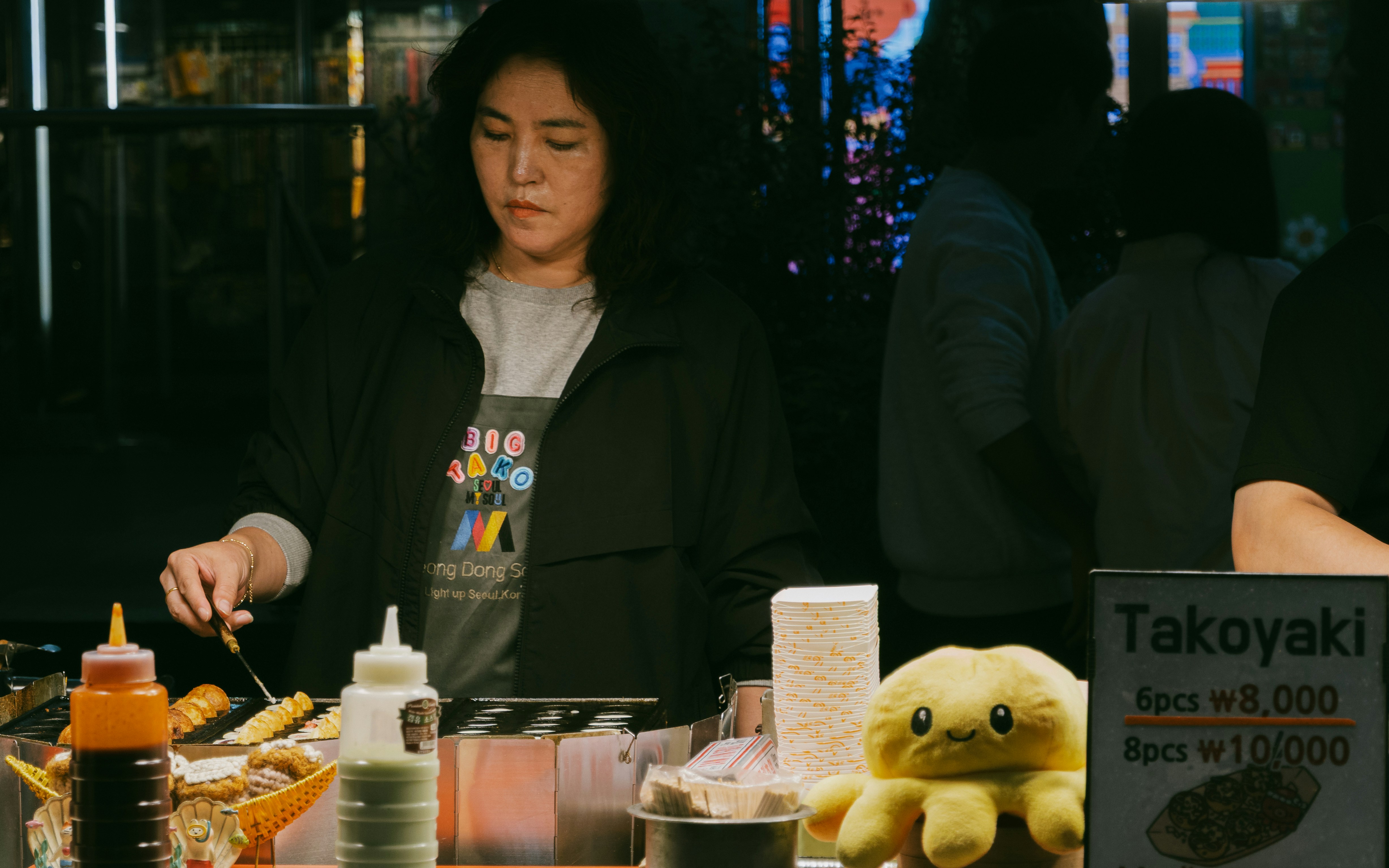 Woman cooking takoyaki at a street food stall.