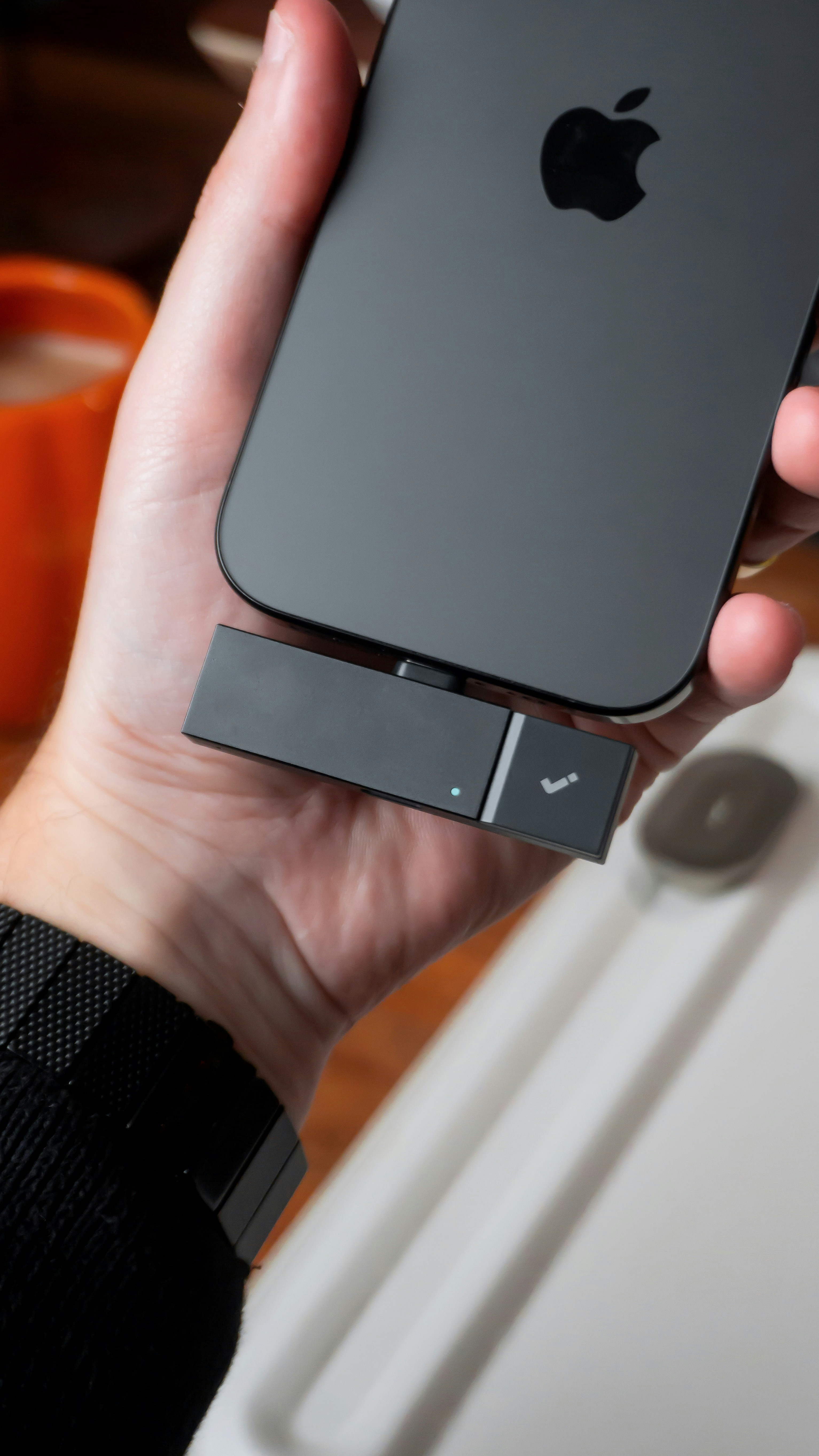 Hand holding iPhone with attachment and coffee cup.