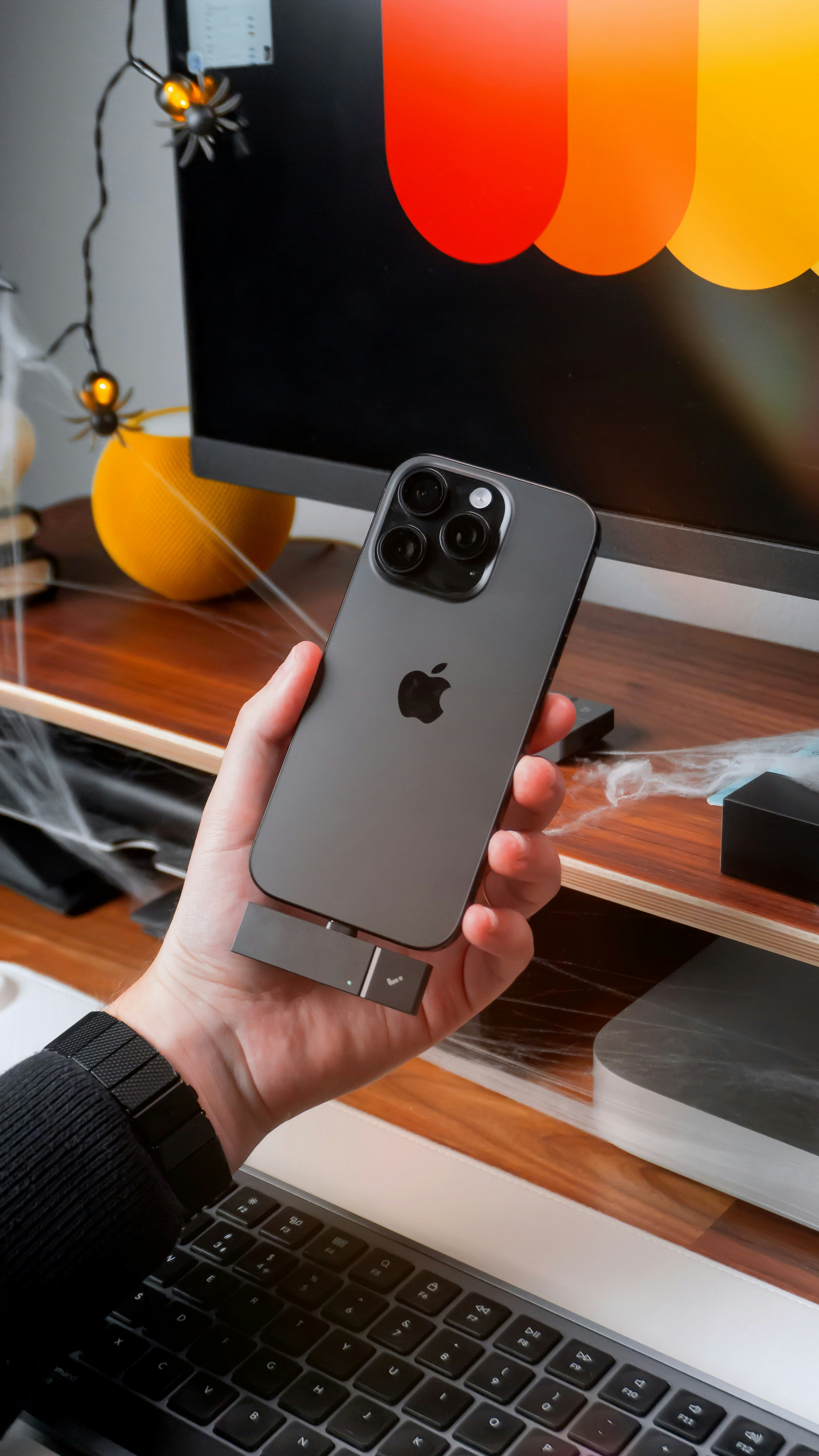 Hand holding iPhone with adapter near computer keyboard.