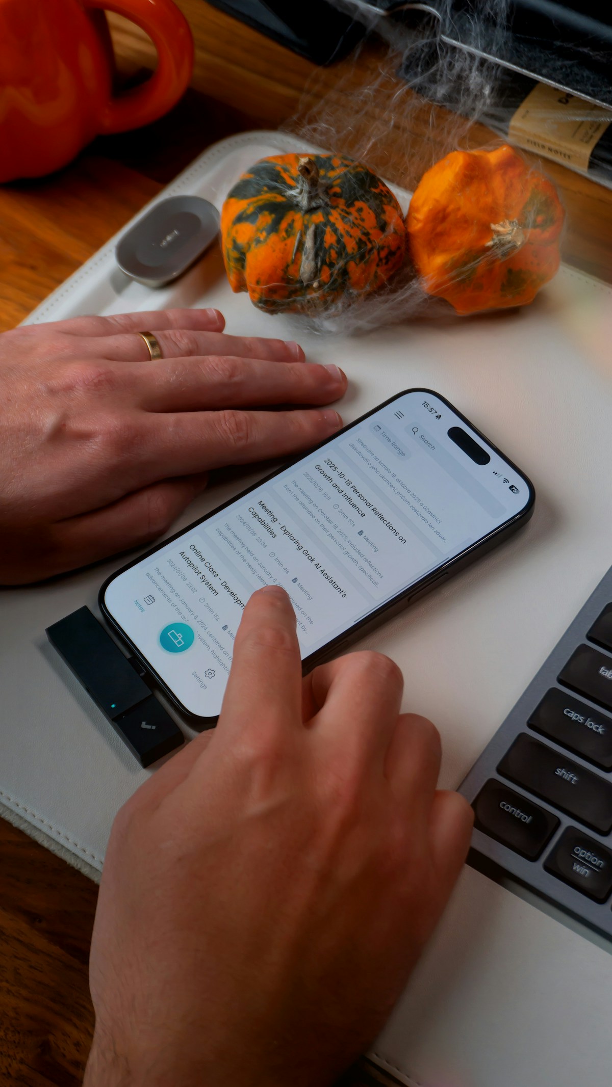 Hands using a smartphone next to pumpkins and keyboard