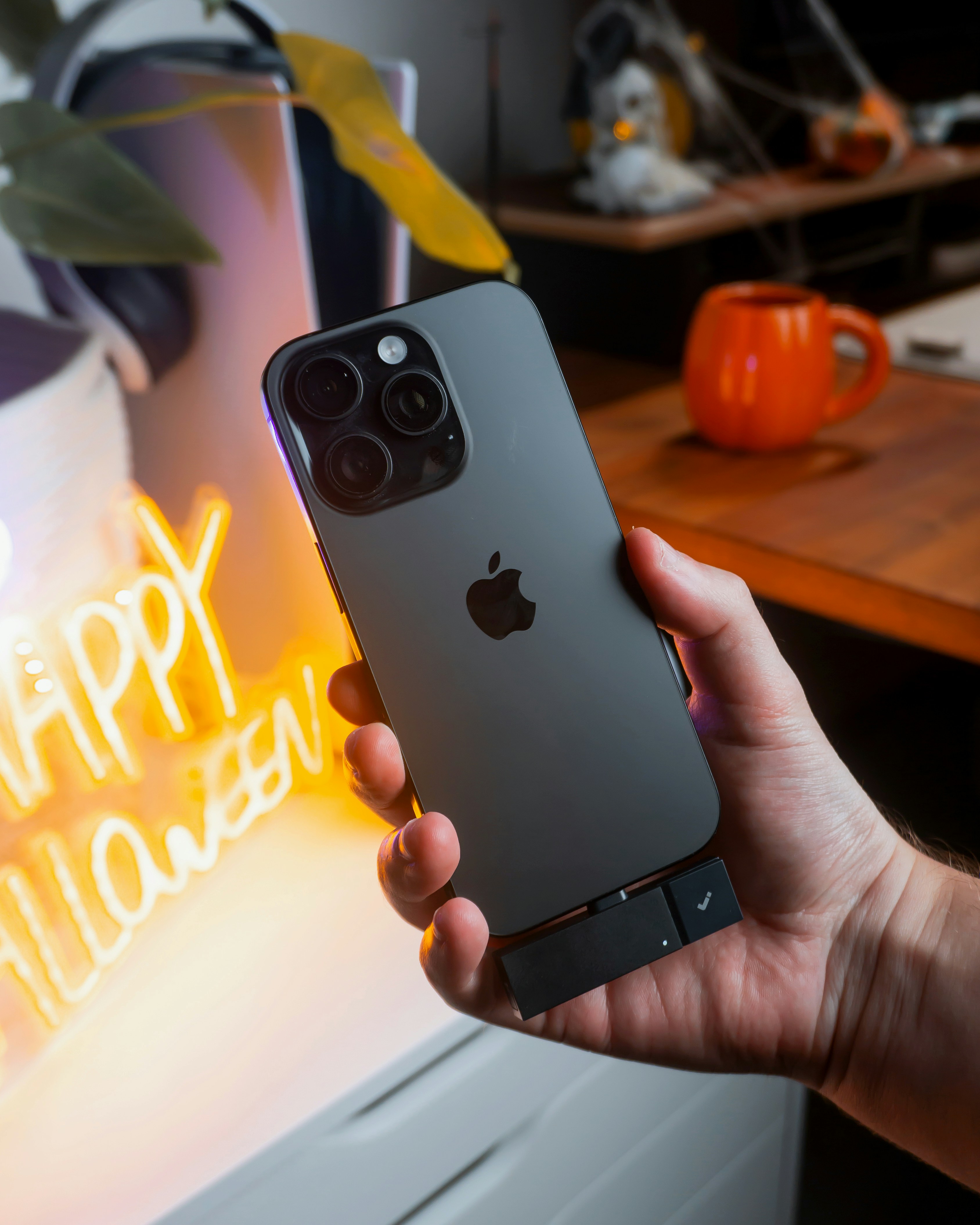 Hand holding a dark grey iPhone with camera lenses.