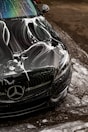 Black car covered in soap suds during wash.