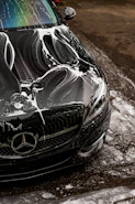 Black car covered in soap suds during wash.
