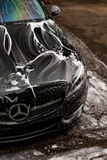 Black car covered in soap suds during wash.