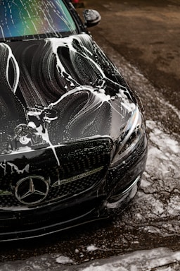 Black car covered in soap suds during wash.