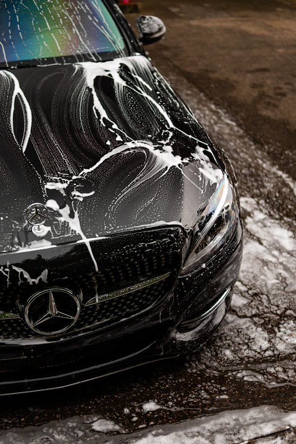 Black car covered in soap suds during wash.