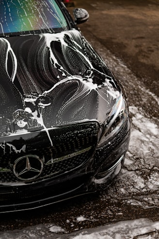 Black car covered in soap suds during wash.