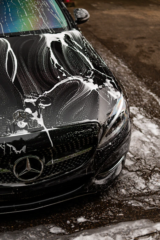 Black car covered in soap suds during wash.