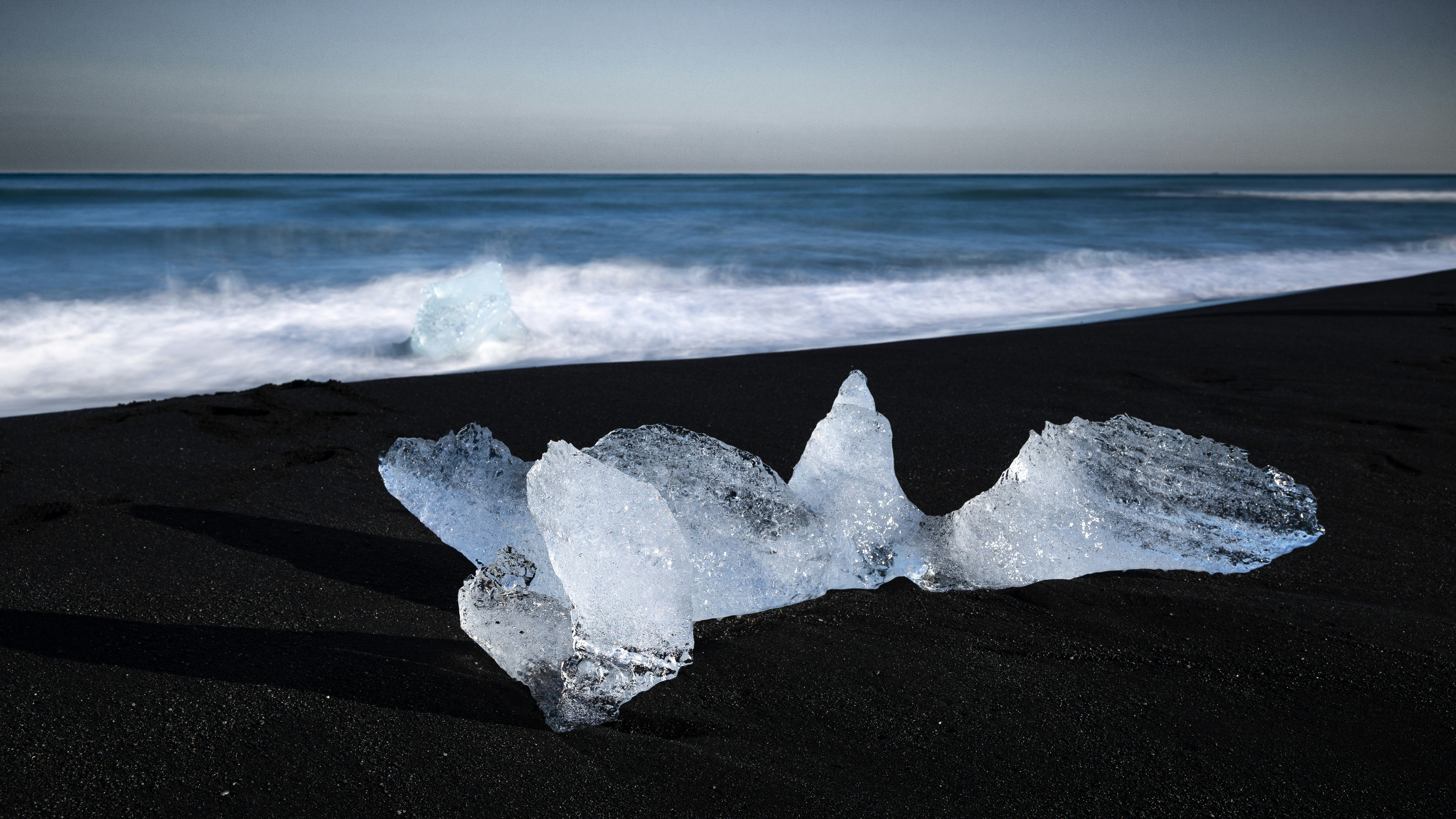 Eisbrocken an einem schwarzen Sandstrand mit Meereswellen.