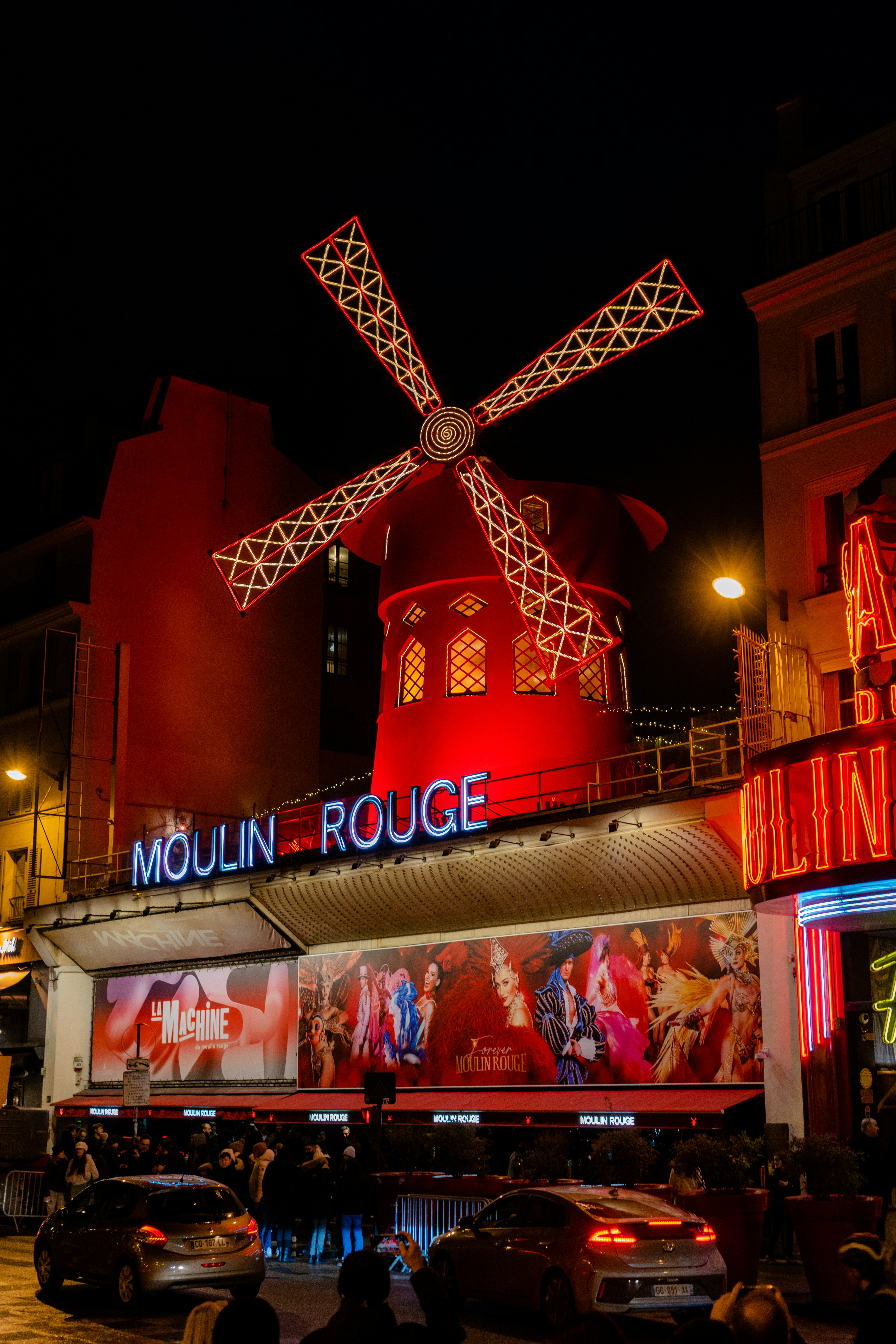 Foto noturna do moinho do Moulin Rouge e da fachada iluminada do cabaré em Paris, França.