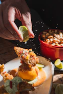 Hand squeezing lime over fried food with sauce and garnish