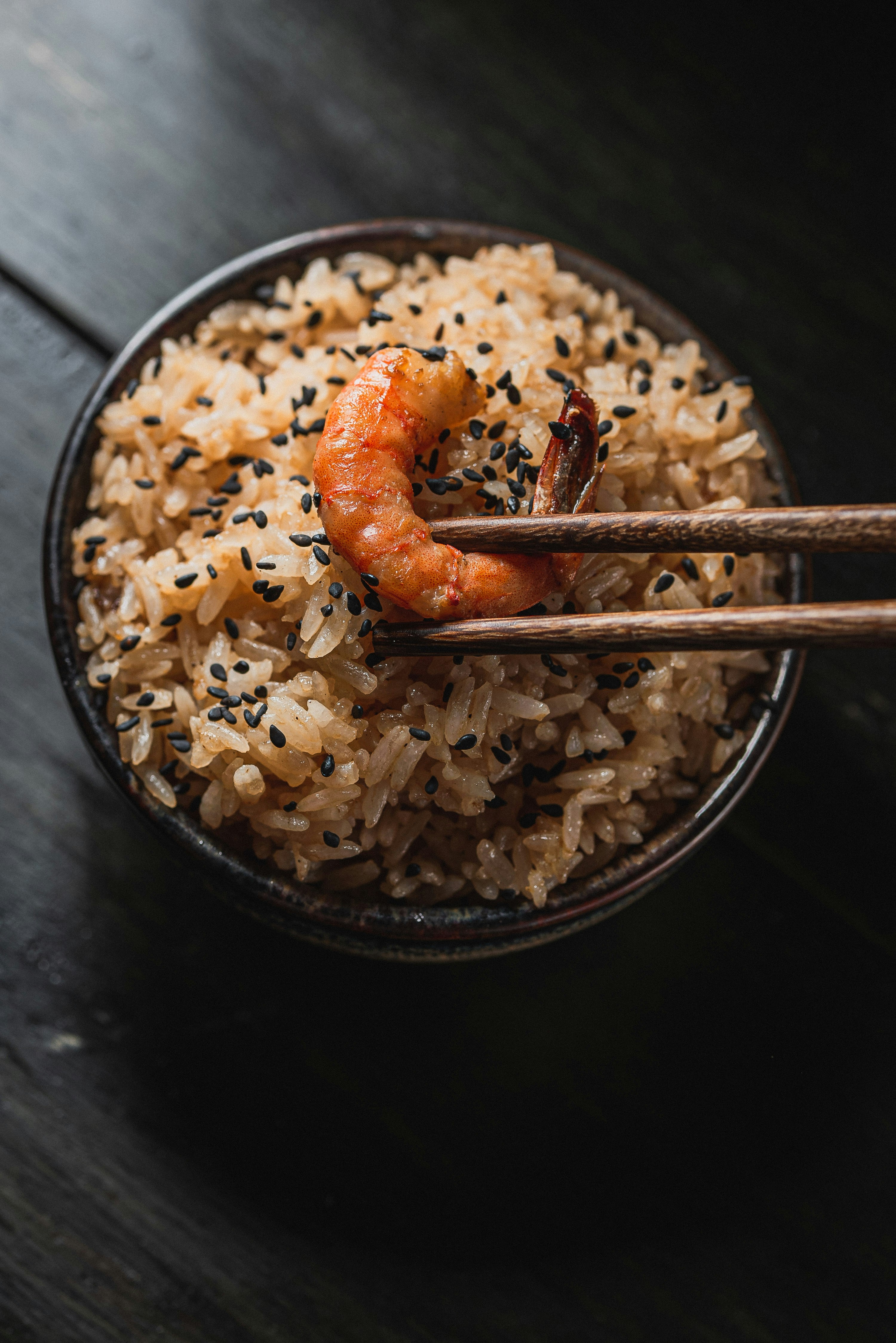 Chopsticks holding shrimp over bowl of rice