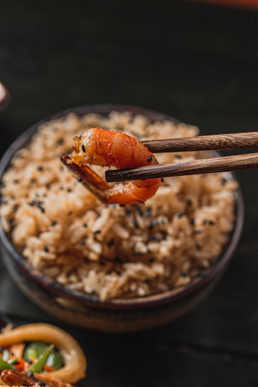 Chopsticks holding a shrimp over rice