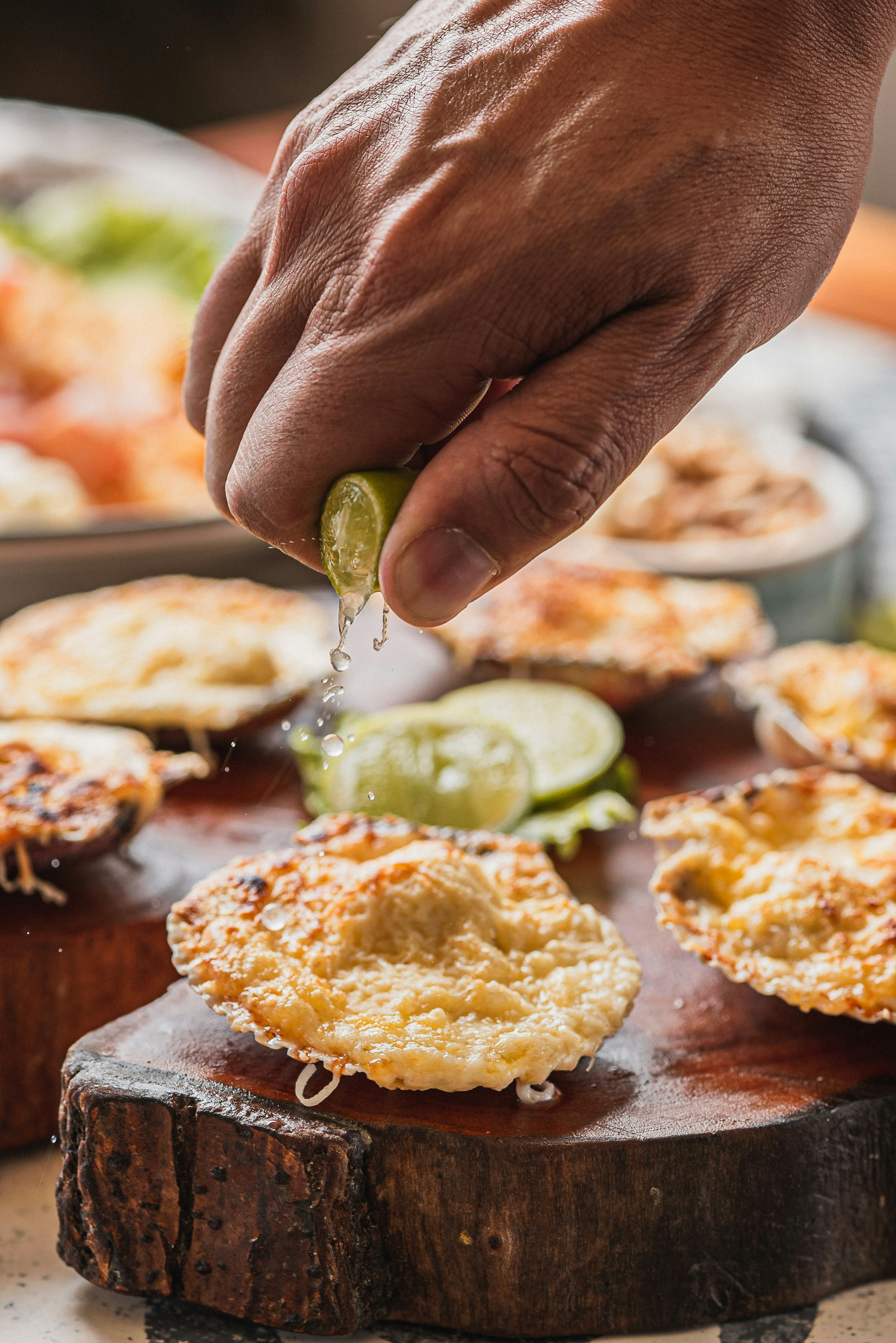 Hand squeezing lime over baked scallops with cheese scallops.