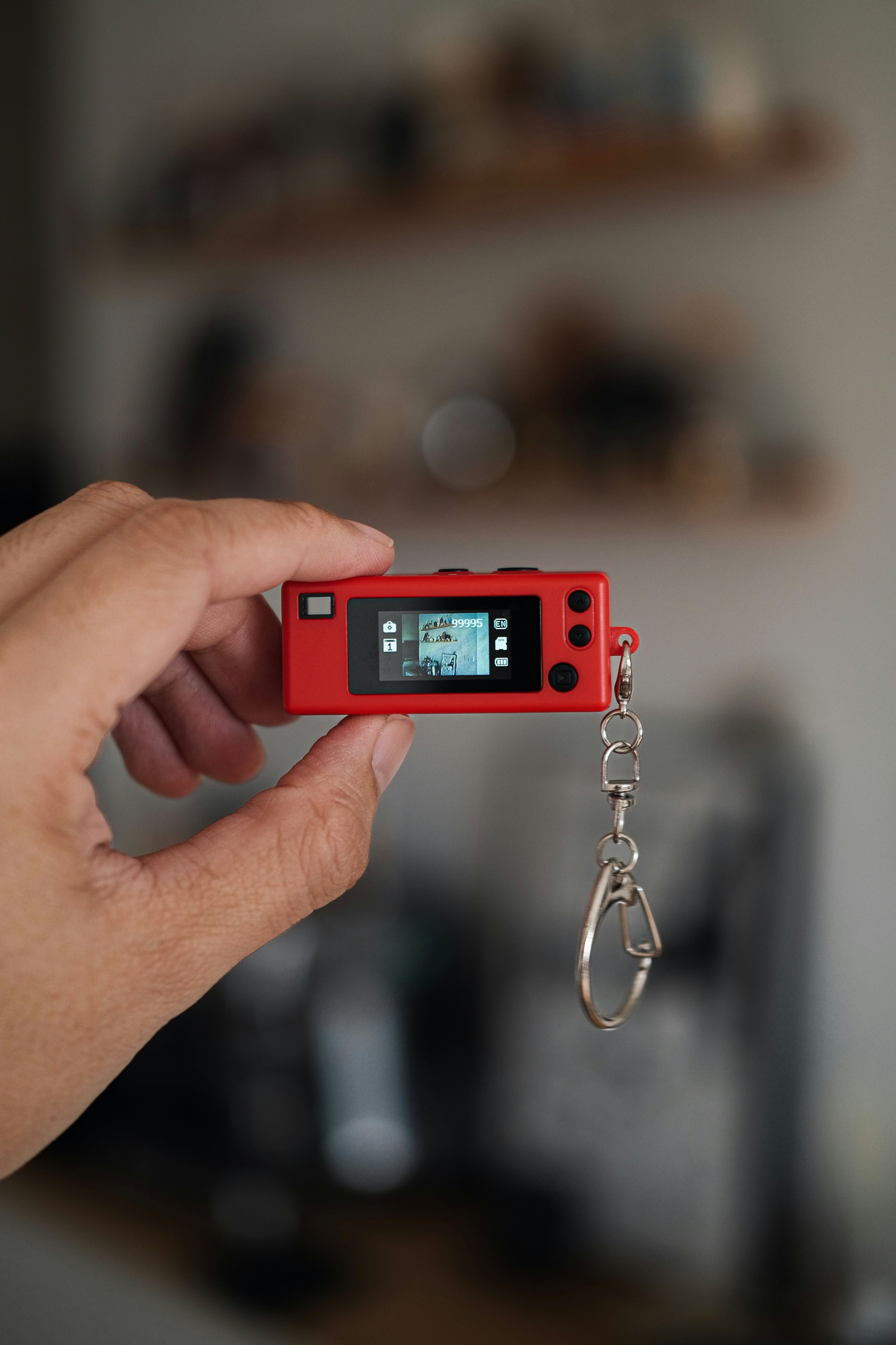 Hand holding a tiny red digital camera with keychain.