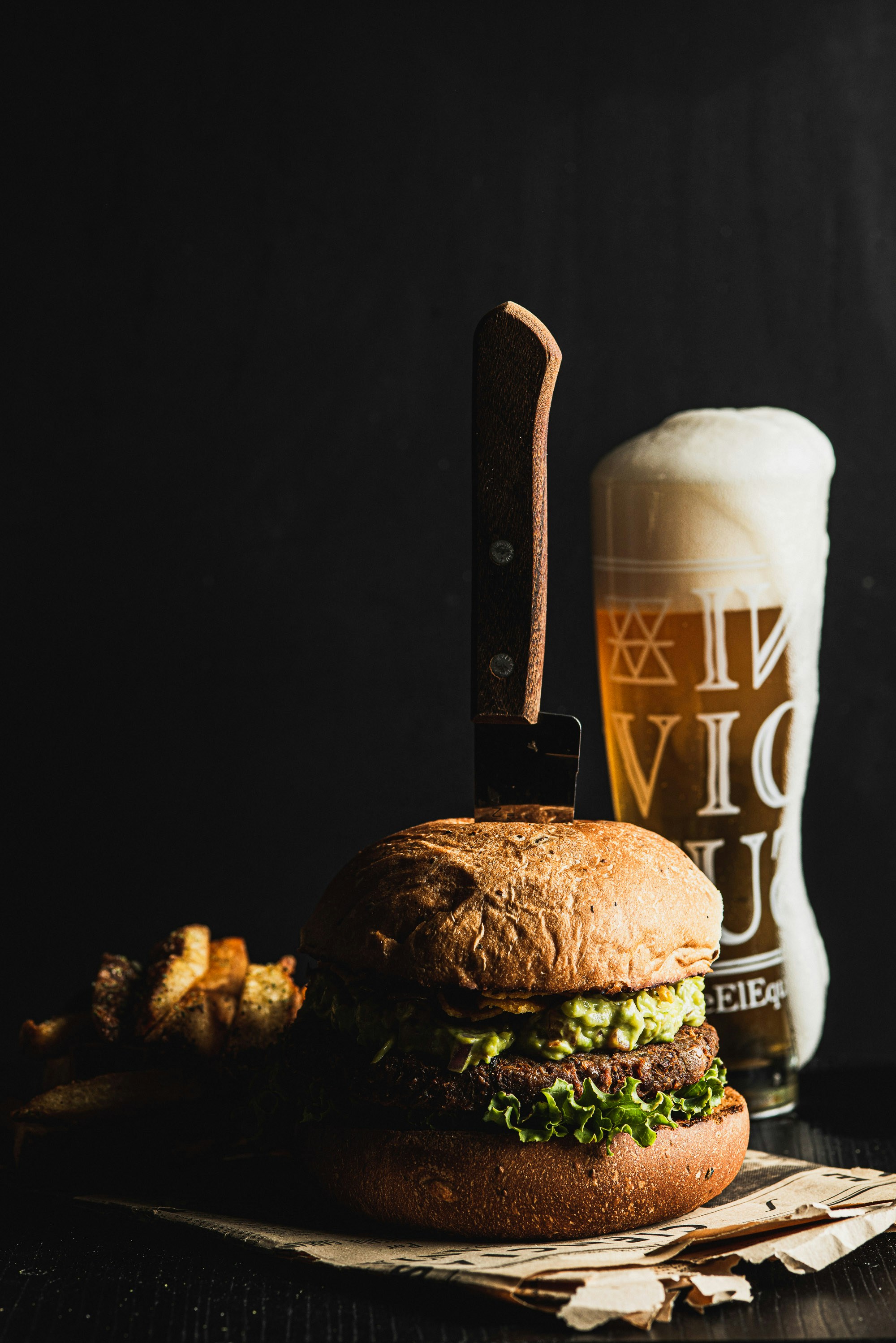 Burger with knife, fries, and beer on dark background
