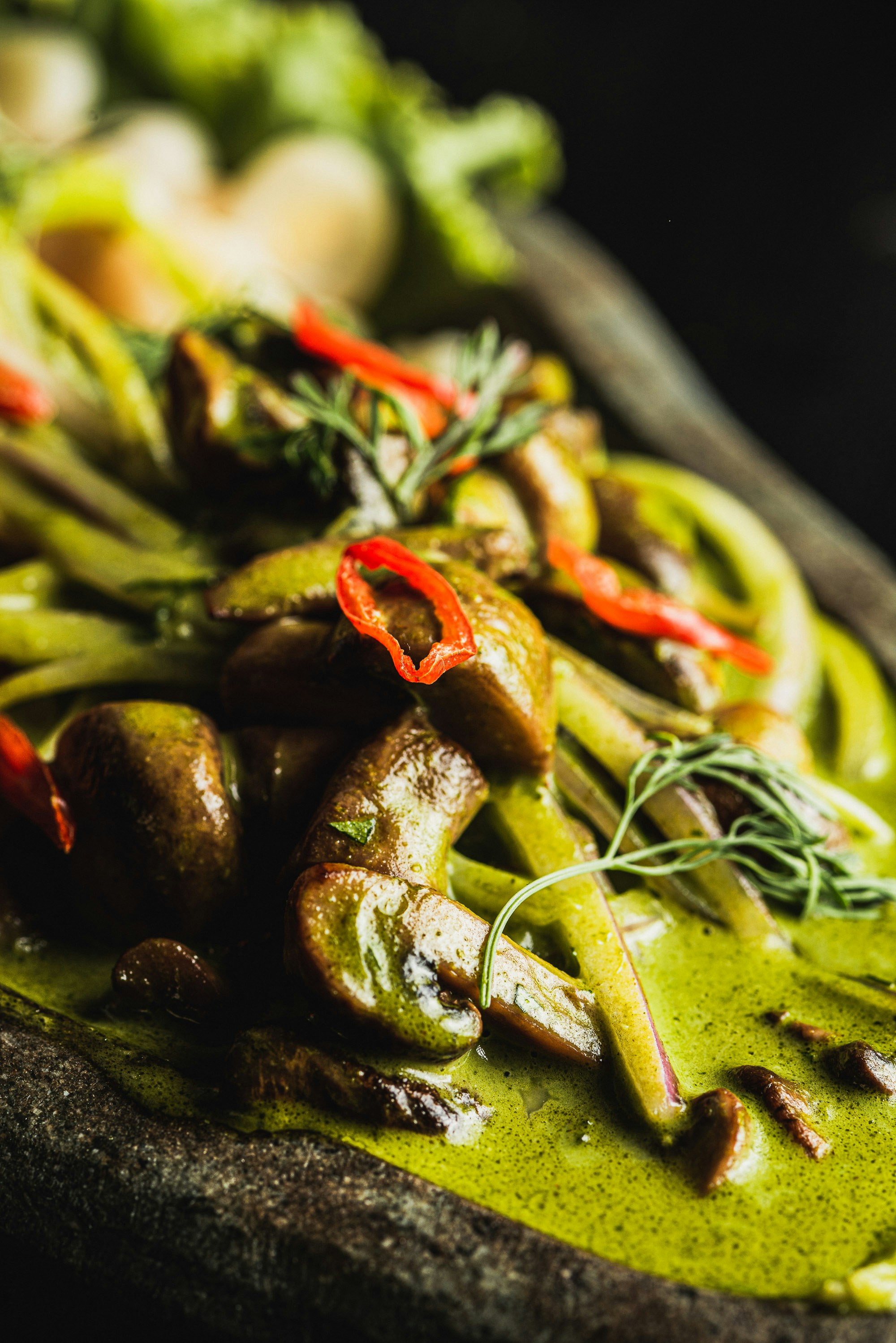 A close-up of a green curry with mushrooms and chili.