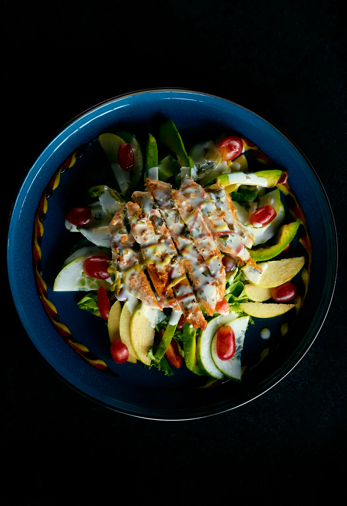 Grilled chicken salad with avocado and tomatoes in a dark bowl