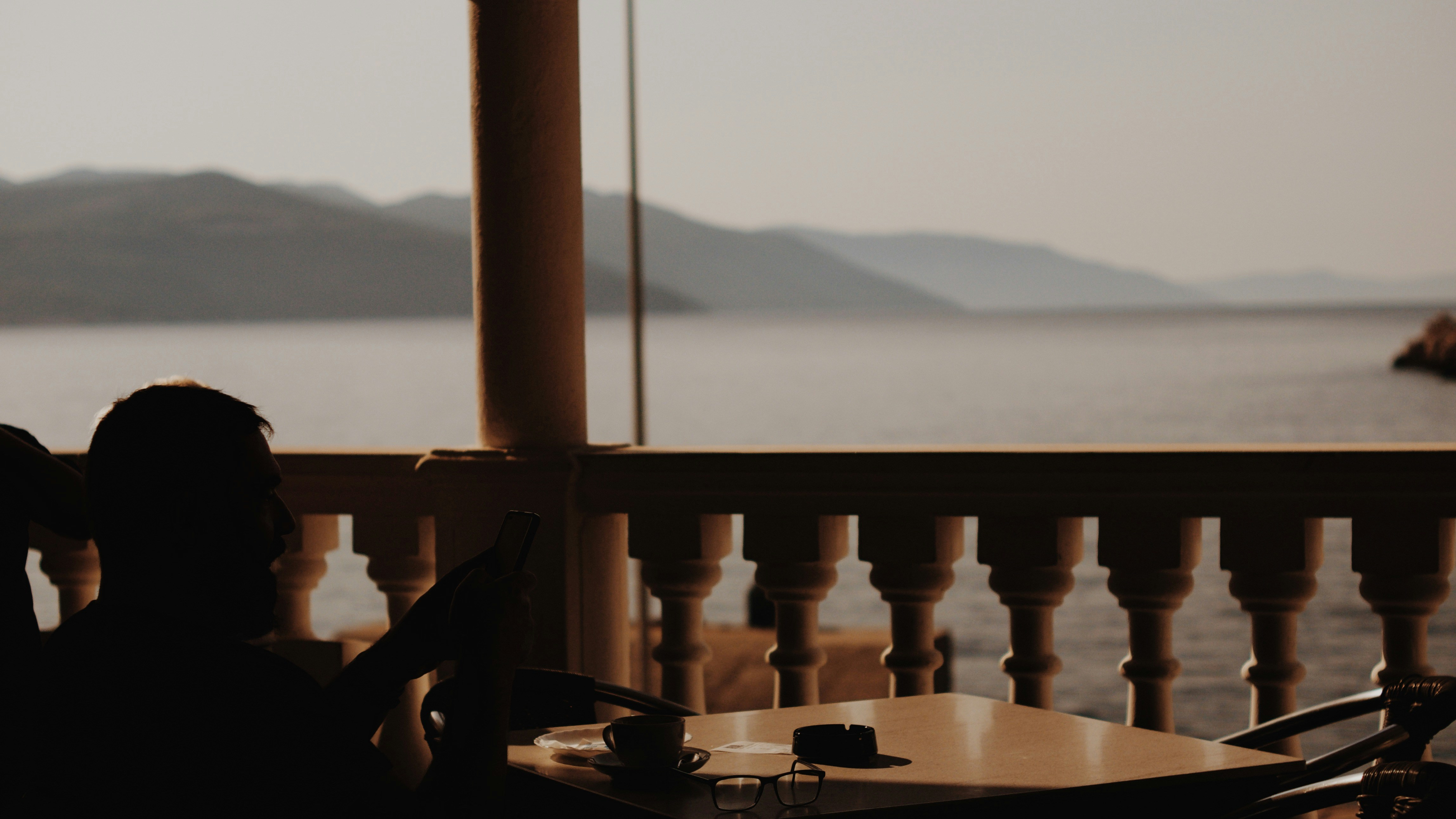 Silhouetted figures at a table overlooking the sea.