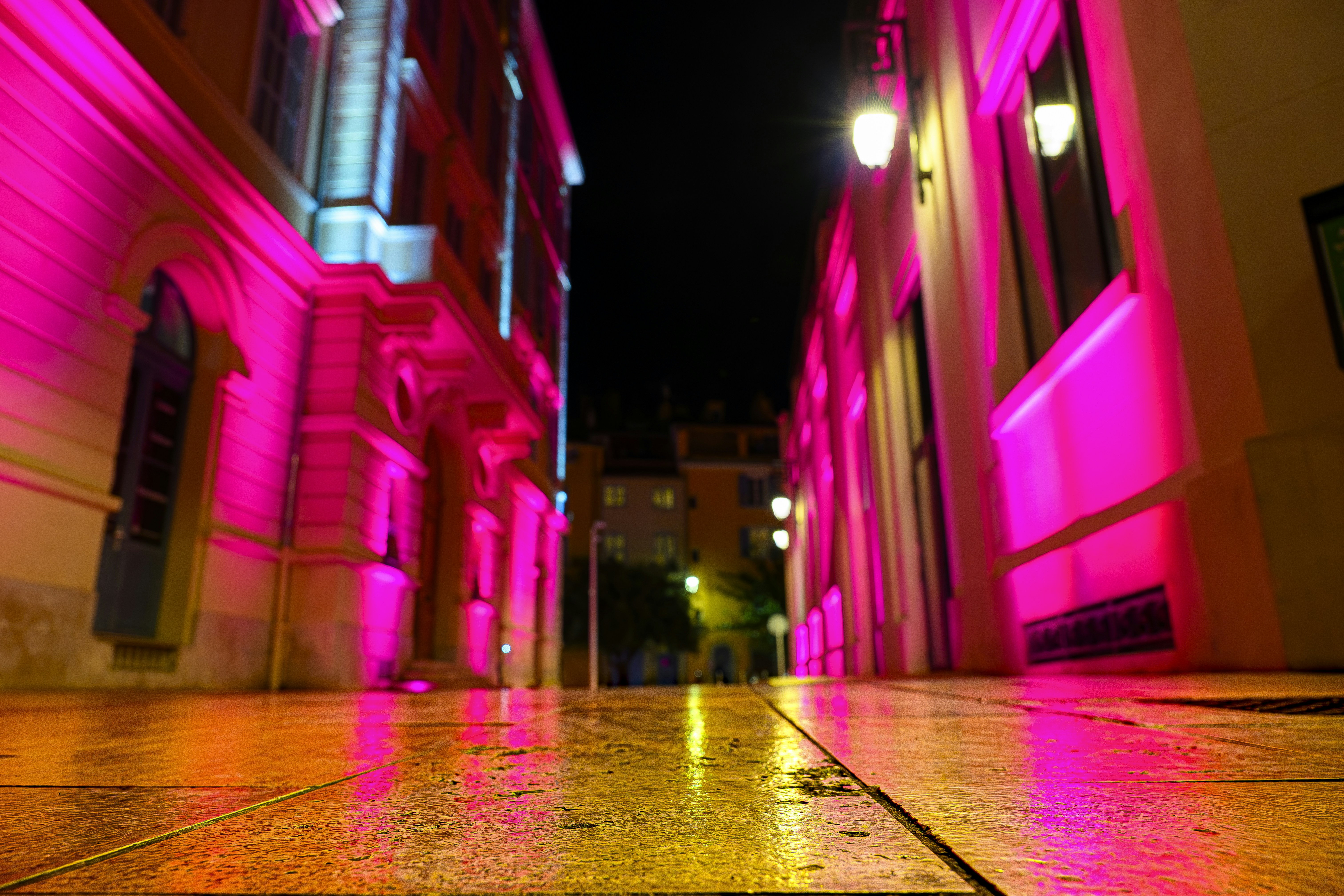 A narrow street illuminated by vibrant pink lights at night.