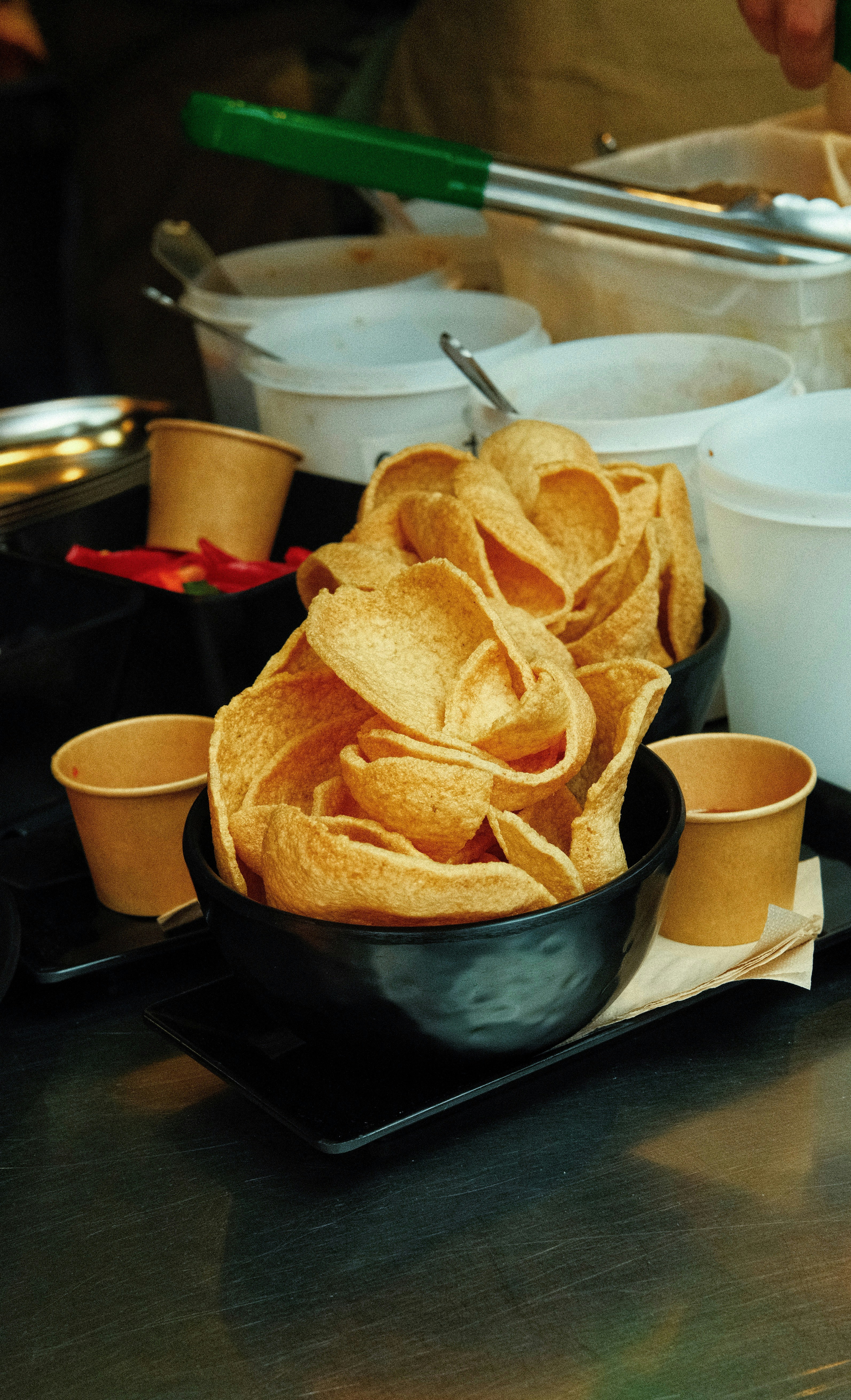 Crispy snacks piled in a black bowl with cups.