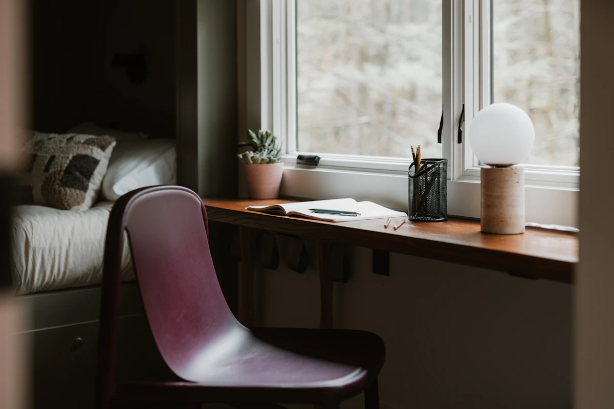A chair and desk by a window with a lamp.