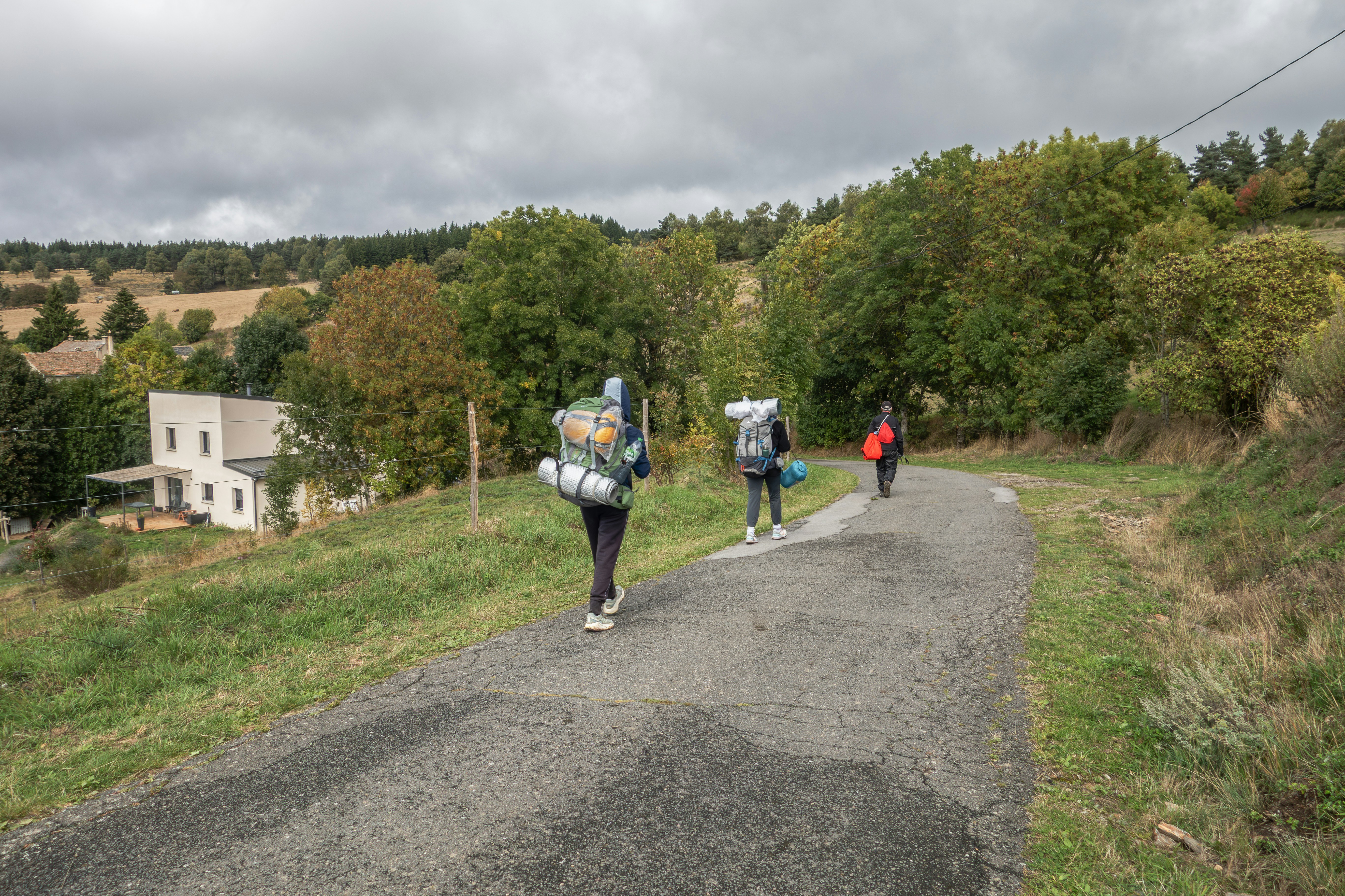 Three hikers with large backpacks walk up a rural road.
