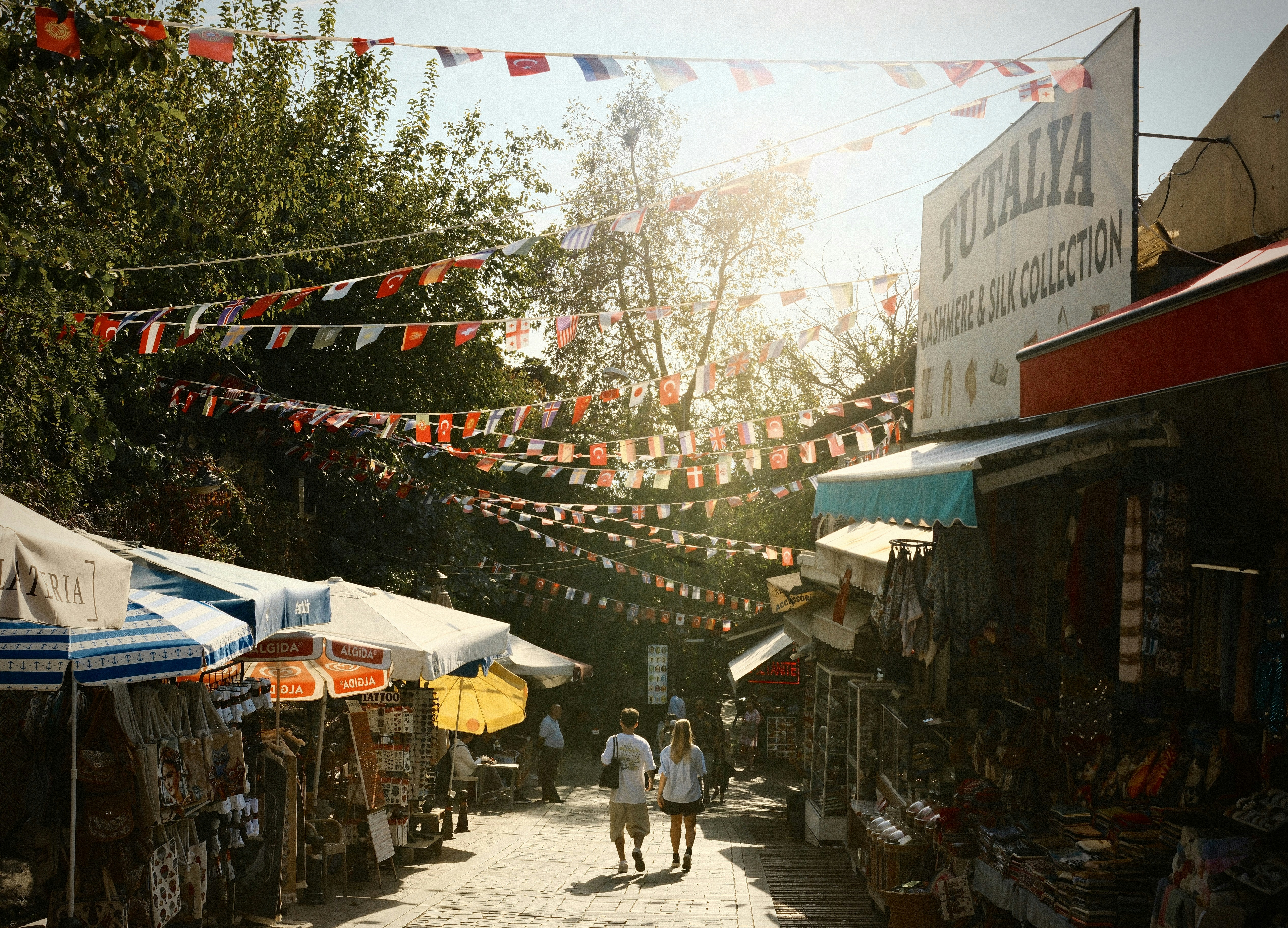 La gente camina por una soleada calle del mercado con banderas.