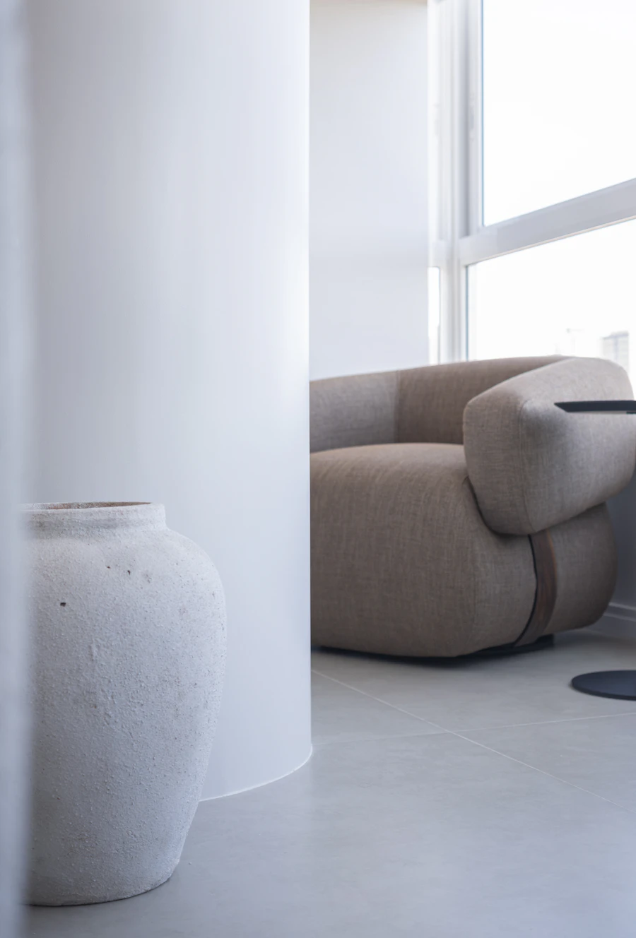 A soft curved armchair and a stone vase in a bright, quiet room