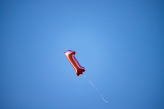 A single red balloon floats in a clear blue sky.