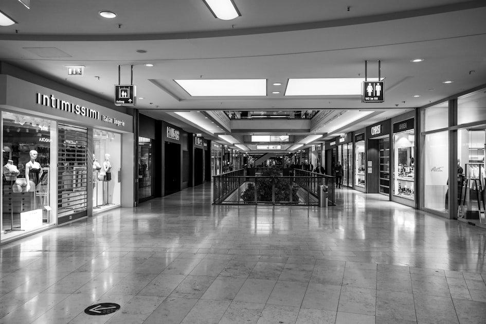 An empty shopping mall corridor lined with open storefronts and no shoppers walking through it, representing agentic commerce infrastructure built ahead of the buyers it was meant to serve