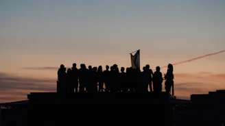 Silhouetted crowd on rooftop against colorful sunset sky