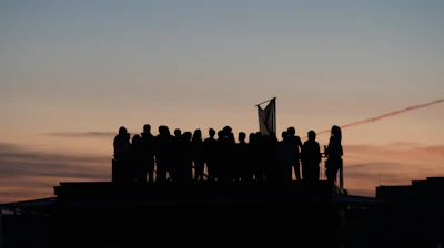 Silhouetted crowd on rooftop against colorful sunset sky
