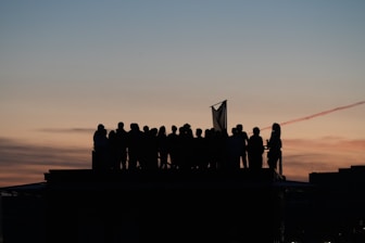 Silhouetted crowd on rooftop against colorful sunset sky