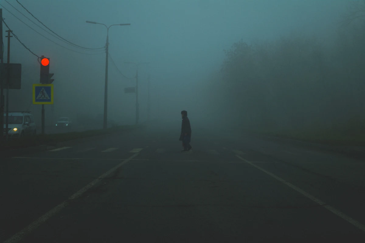 A person crossing a foggy street at night